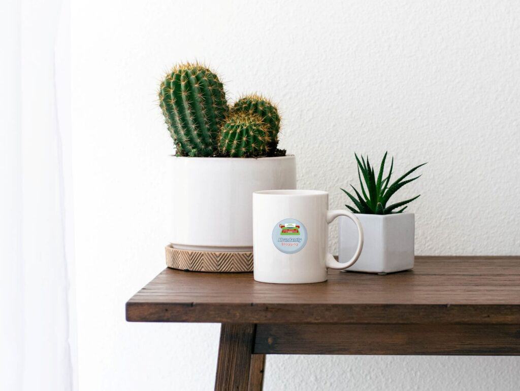 a brown table against the white wall with 2 cacti on it and a white mug with the Abundantly Blogging logo - How to repurpose