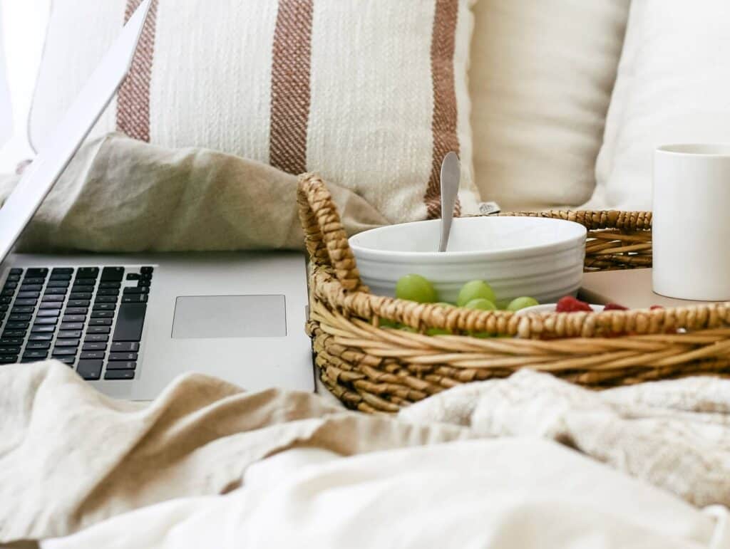a cozy setting of an open laptop and tray with breakfast on a bed - morning routine for bloggers