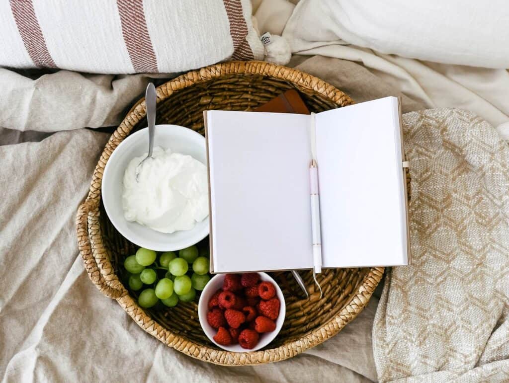 a cozy setting of a tray with breakfast and an open notebook with pen on a bed - morning routine for bloggers