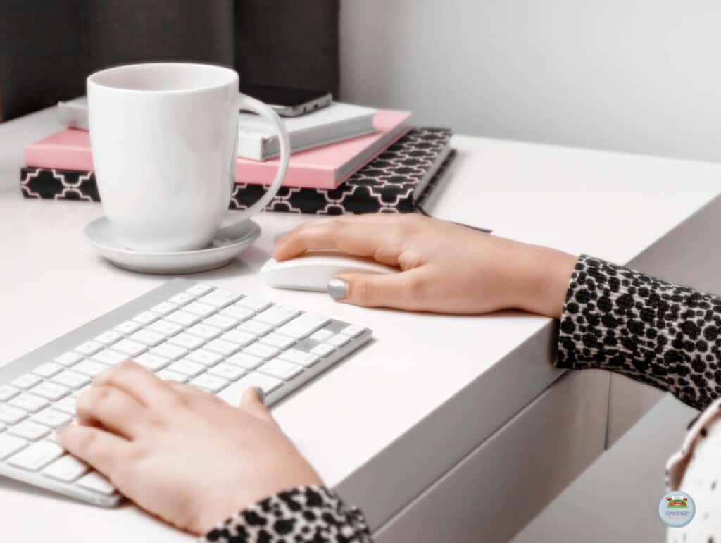 A woman is working at a white desk with a modern keyboard and mouse. There is a cup of coffee and three notebooks with a phone on top - Setting Realistic Deadlines