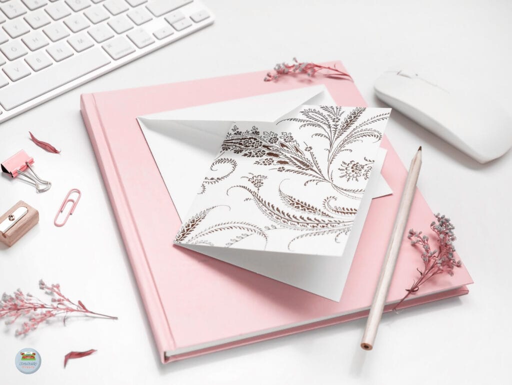 A white desk with a modern keyboard and mouse plus a notebook with on top a envelop, a card and a pencil. Around are some clips and flowers - Setting Realistic Deadlines