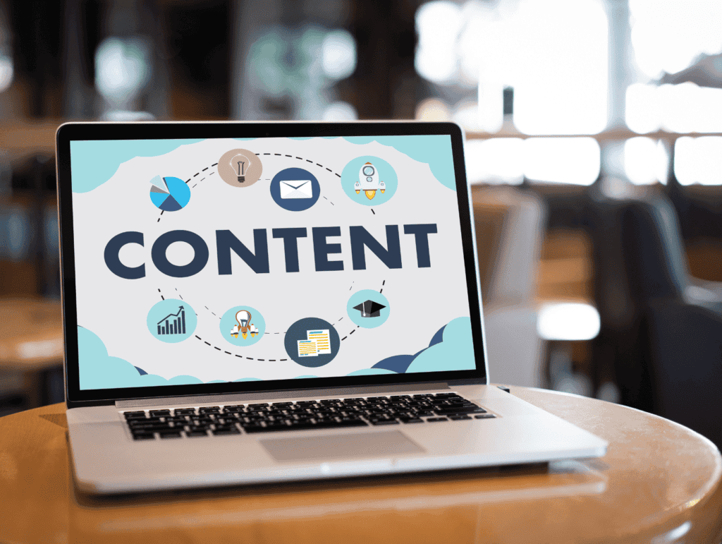 an open laptop on a round table in a café. The screen on the laptop has the word content with some symbols around it - celebrating blogging milestones