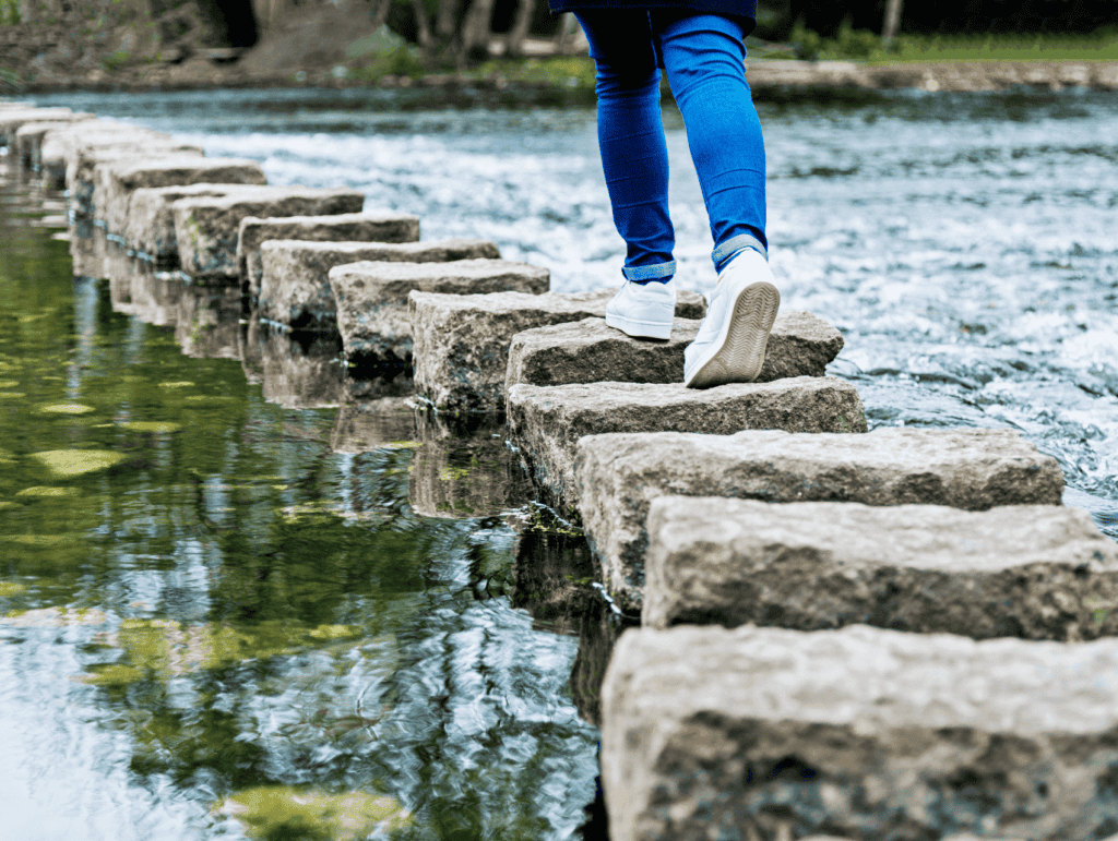 big natural stepping stones in a river or lake. There is a woman going over the stepping stones - celebrating blogging milestones