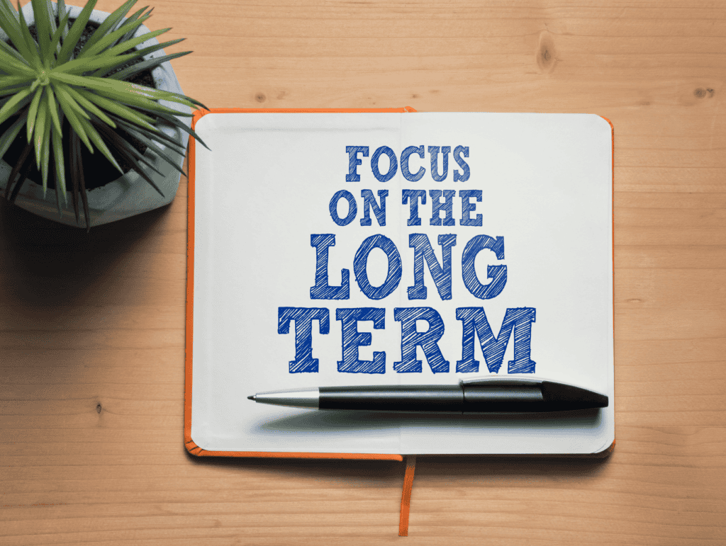 An open orange notebook, a pen, and a succulent on a table. In the notebook it says: Focus on the long term - long-term blogging goals