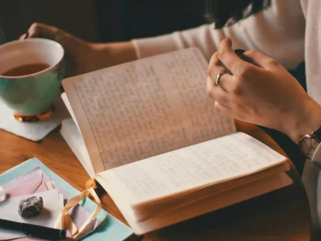a woman sitting at her desk with her journal, a cup of tea and some sweets - time management tips for bloggers