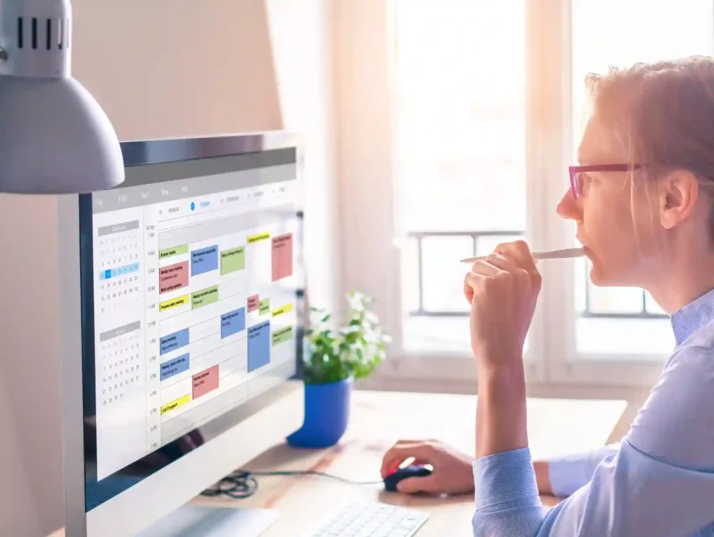 A woman with glasses focuses intently on a computer screen displaying a colorful calendar or scheduling software, demonstrating effective time management and planning. - habits to boost productivity