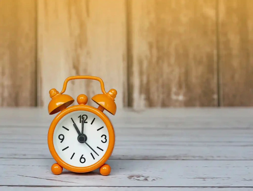 A bright orange alarm clock showing 11:00 stands on a weathered wooden surface against a rustic background, emphasizing the importance of time management for productivity. - habits to boost productivity