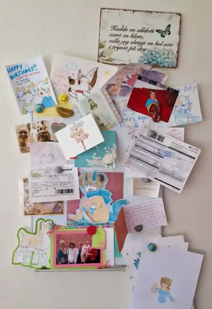 A collection of colorful cards, photos, and personal mementos arranged on a wall, including a decorative sign with an inspirational message - optimize your physical workspace.