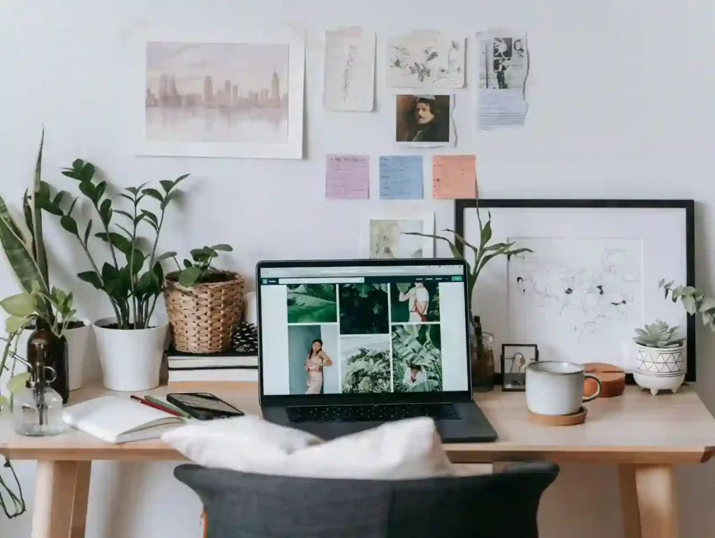 A well-organized desk setup with a laptop displaying a photo collage, surrounded by plants, personal items, and a mood board on the wall, creating an inspiring work environment. - monotasking habit