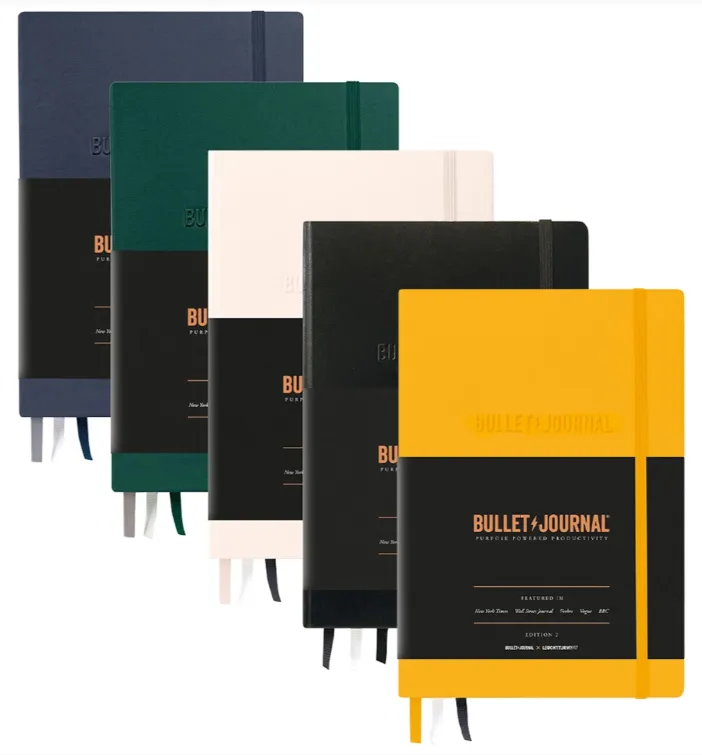 A collection of high-quality bullet journals in various colors including navy blue, forest green, cream, black, and yellow arranged in a diagonal layout - journaling for productivity