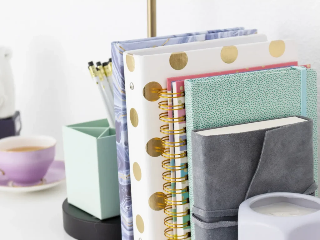 A cozy desk setup featuring organized journals with gold polka dots, a mint green notebook, and a lavender teacup alongside a white instant camera and gold desk accessories - journaling for productivity