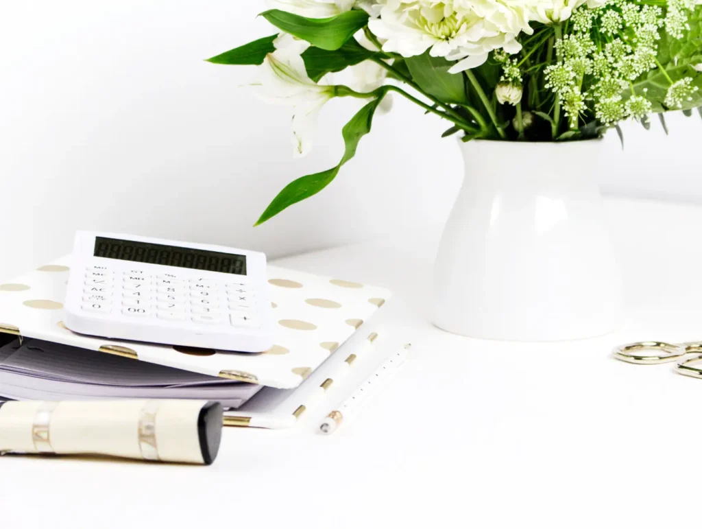 A minimalist white desk setup featuring a white calculator, notebook, and floral arrangement on a polka-dotted surface - brain-dump