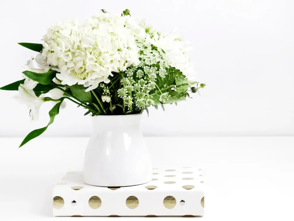 A white ceramic vase filled with white hydrangeas and delicate Queen Anne's lace sits atop a white and gold polka-dotted platform - brain-dump