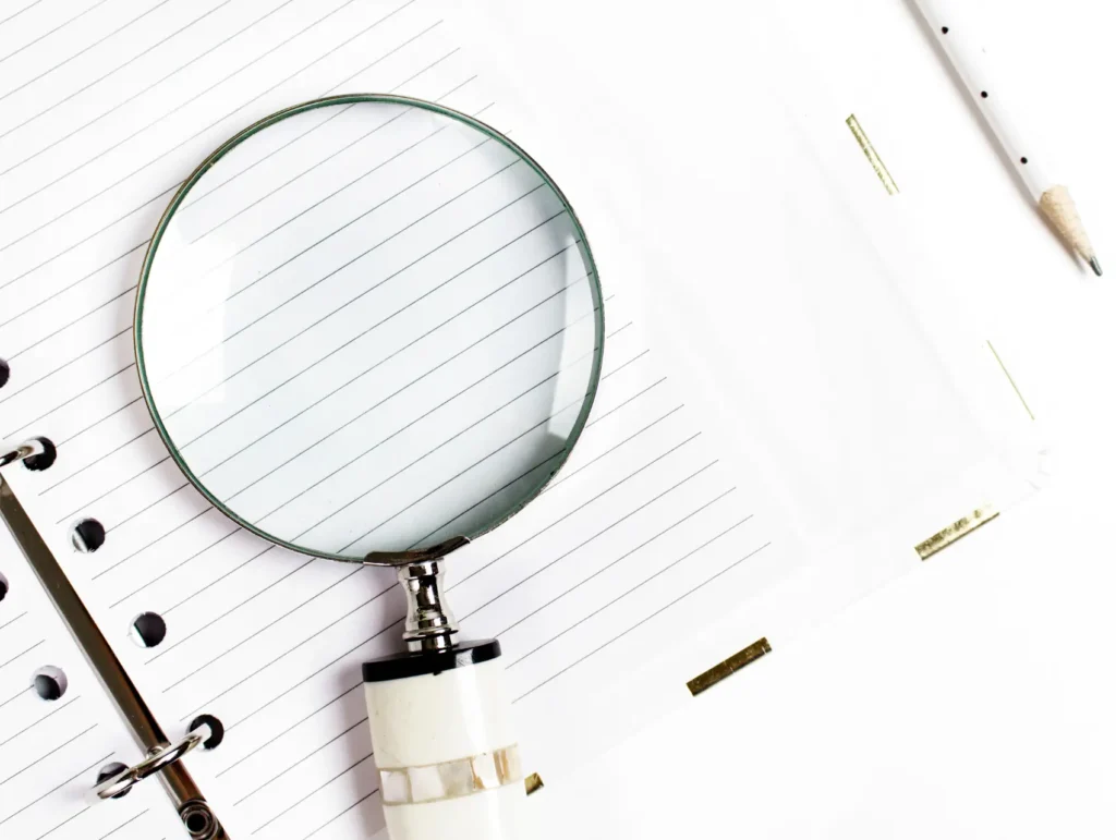 A magnifying glass with a white handle rests on lined notebook paper against a white background - brain-dump