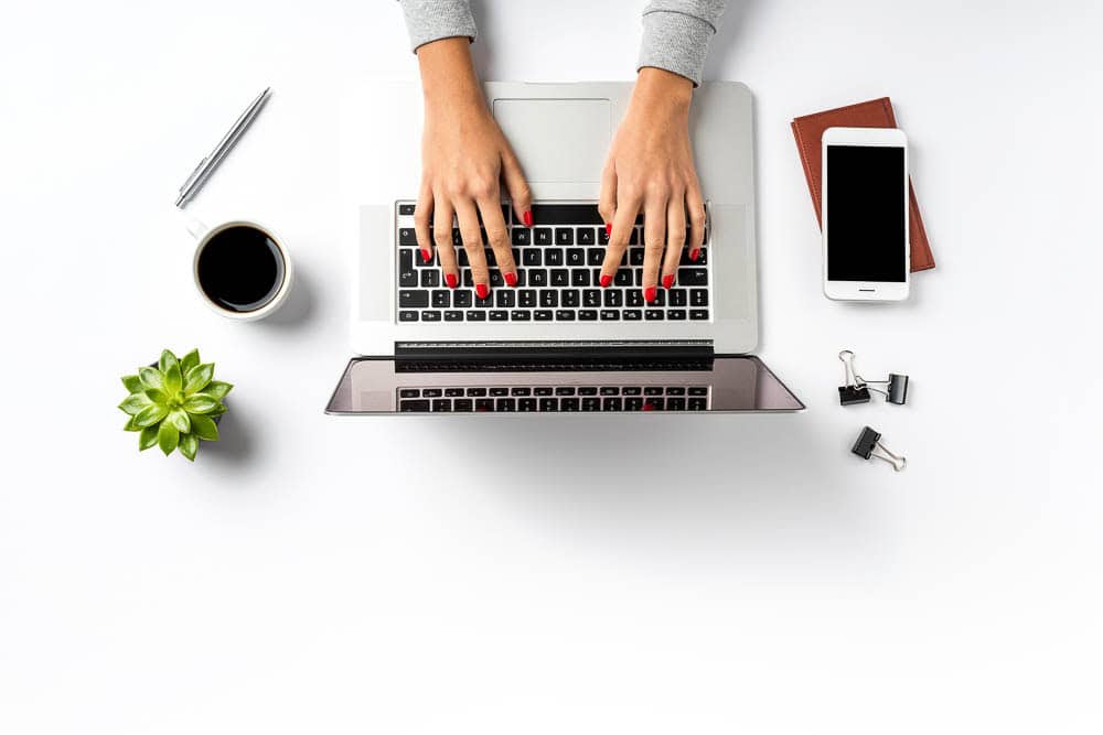Top-down view of a person typing on a laptop at a clean workspace, symbolising digital marketing work.