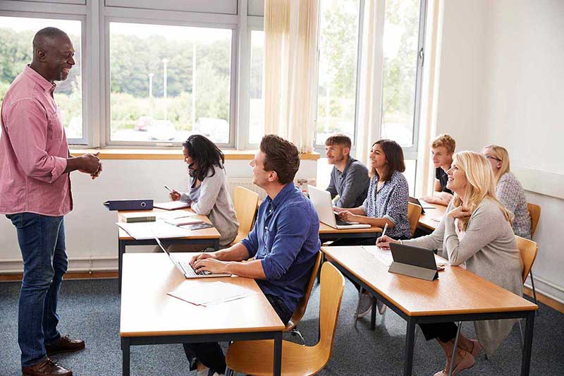 Teacher lecturing adult students in classroom with laptops