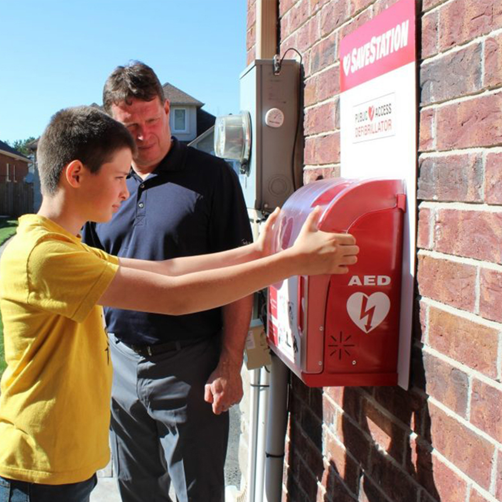 Boy opening AED cabinet with adult supervision