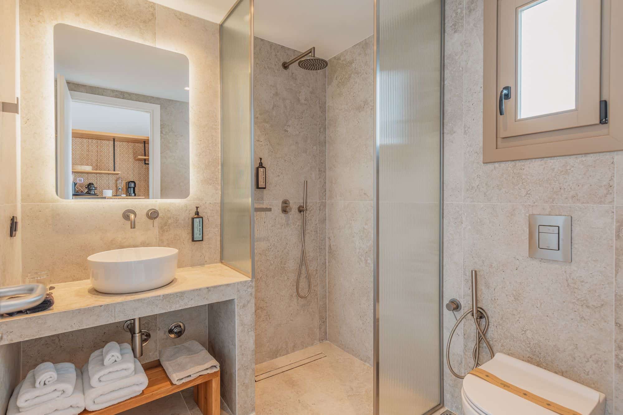 Luxurious bathroom with walk-in shower, stone walls, and contemporary design at Aelo Mykonos.