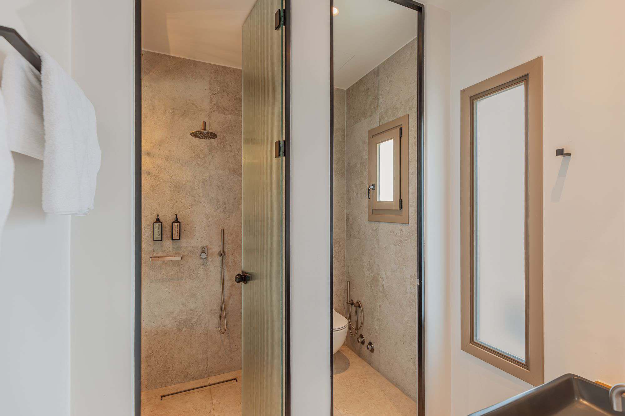 Stylish en-suite bathroom at Aelo Mykonos featuring walk-in shower, beige tiles, and natural light.