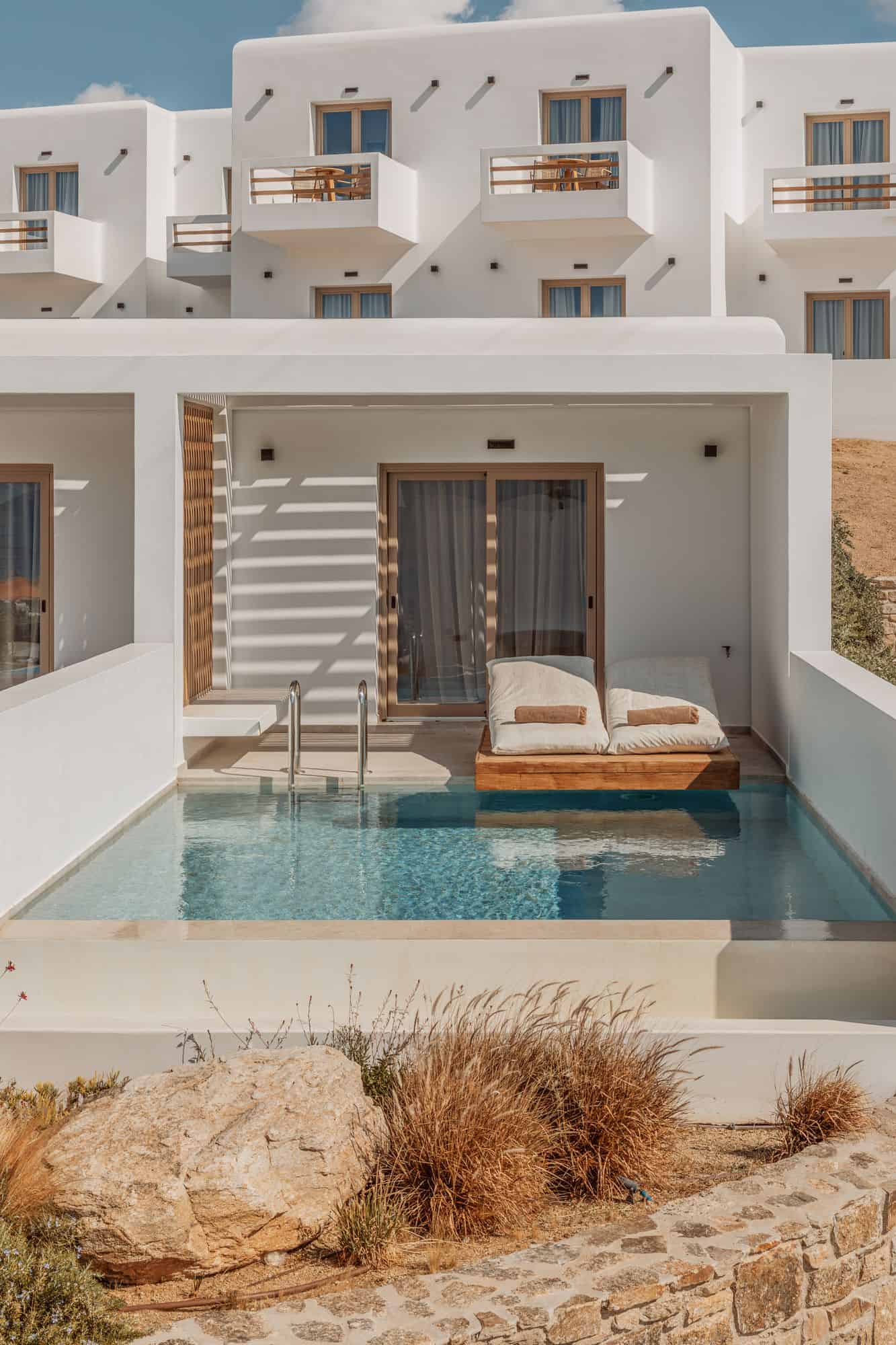 Luxurious white Mykonos villa with pool, sun loungers, and scenic views.
