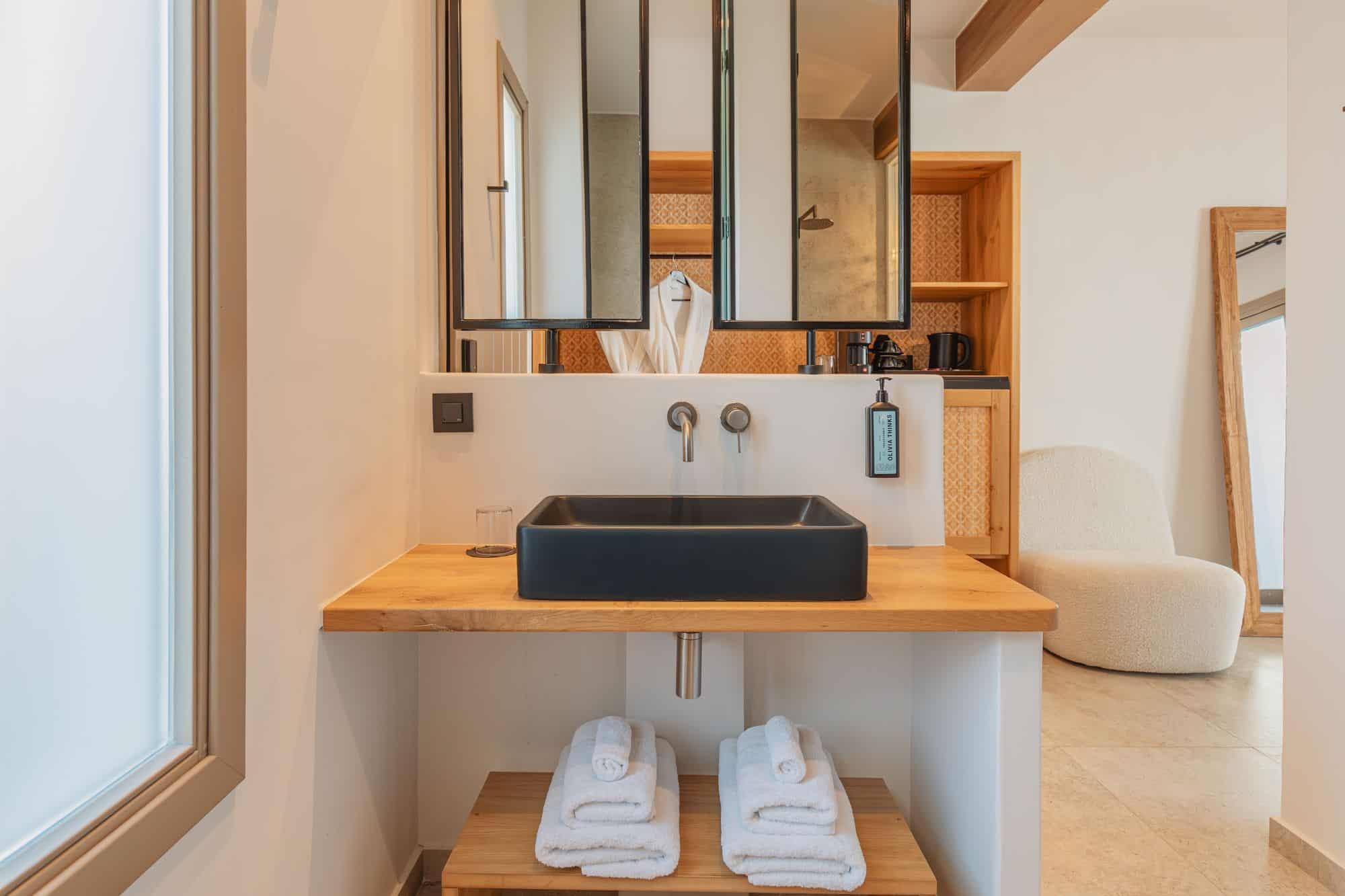 Elegant bathroom with black sink, wooden accents, and plush towels at Aelo Mykonos.