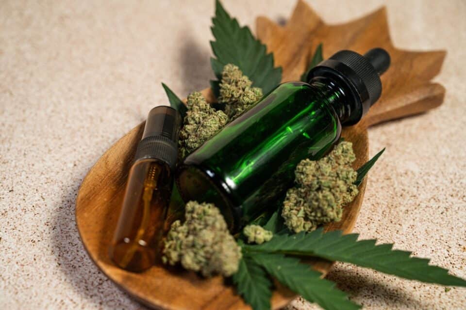 Cannabis flower with tincture and spray bottles displayed on a wooden tray.