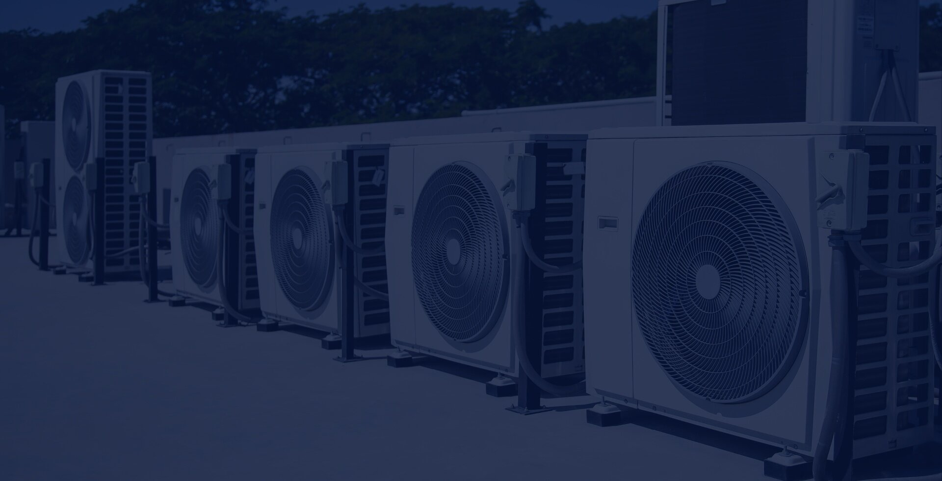 Row of outdoor air conditioning units on a rooftop with trees in the background