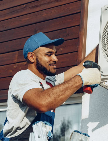 Man in blue cap and work gloves installing an air conditioner unit.