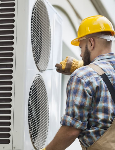 Man in yellow hard hat working on an outdoor air conditioning unit.