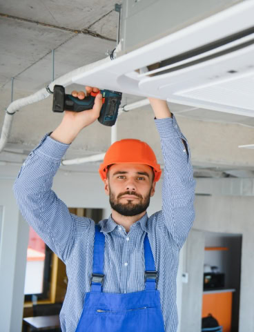 Man in orange hard hat installing an air conditioner with a drill.