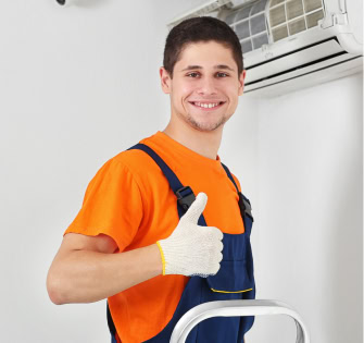 Smiling man in work clothes giving a thumbs up near an air conditioner.