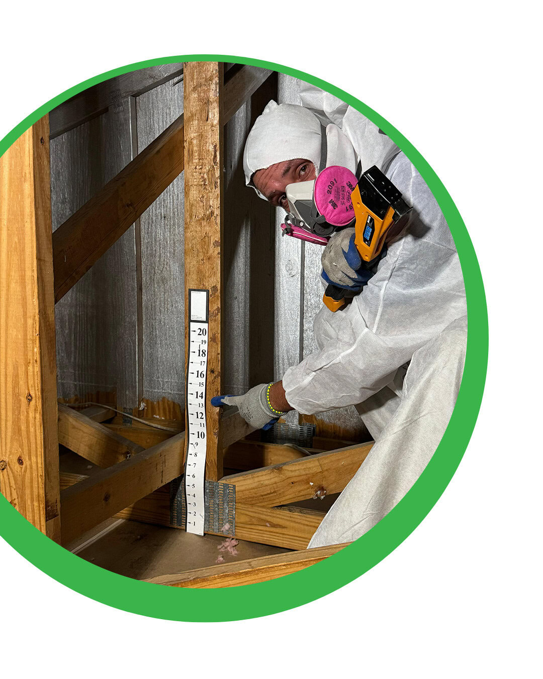 Person in hazmat suit pointing at a measurement stick in an attic.