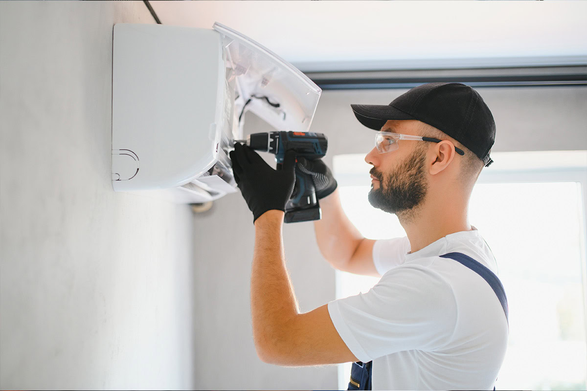Man installing an air conditioner on a wall with a drill.