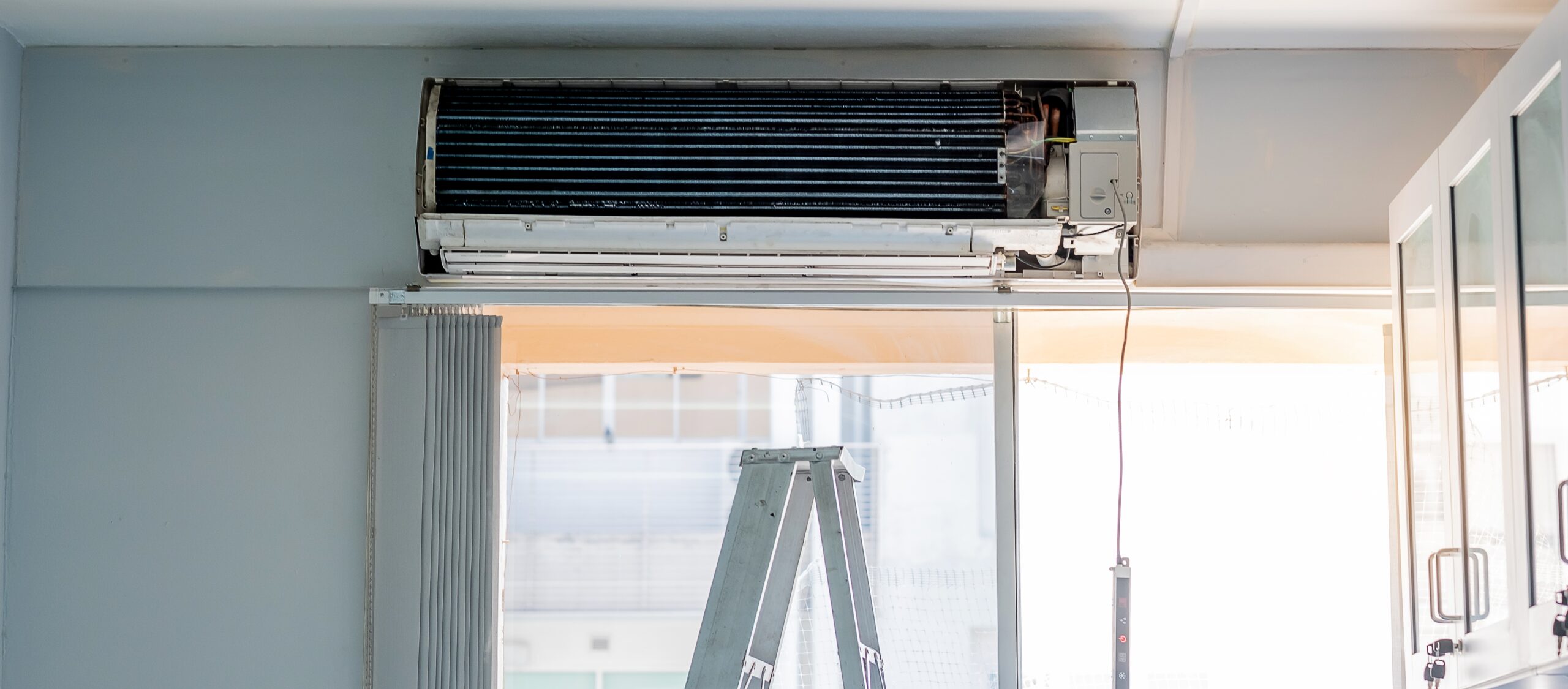 Air conditioner unit with cover removed, showing internal fins, above a window.
