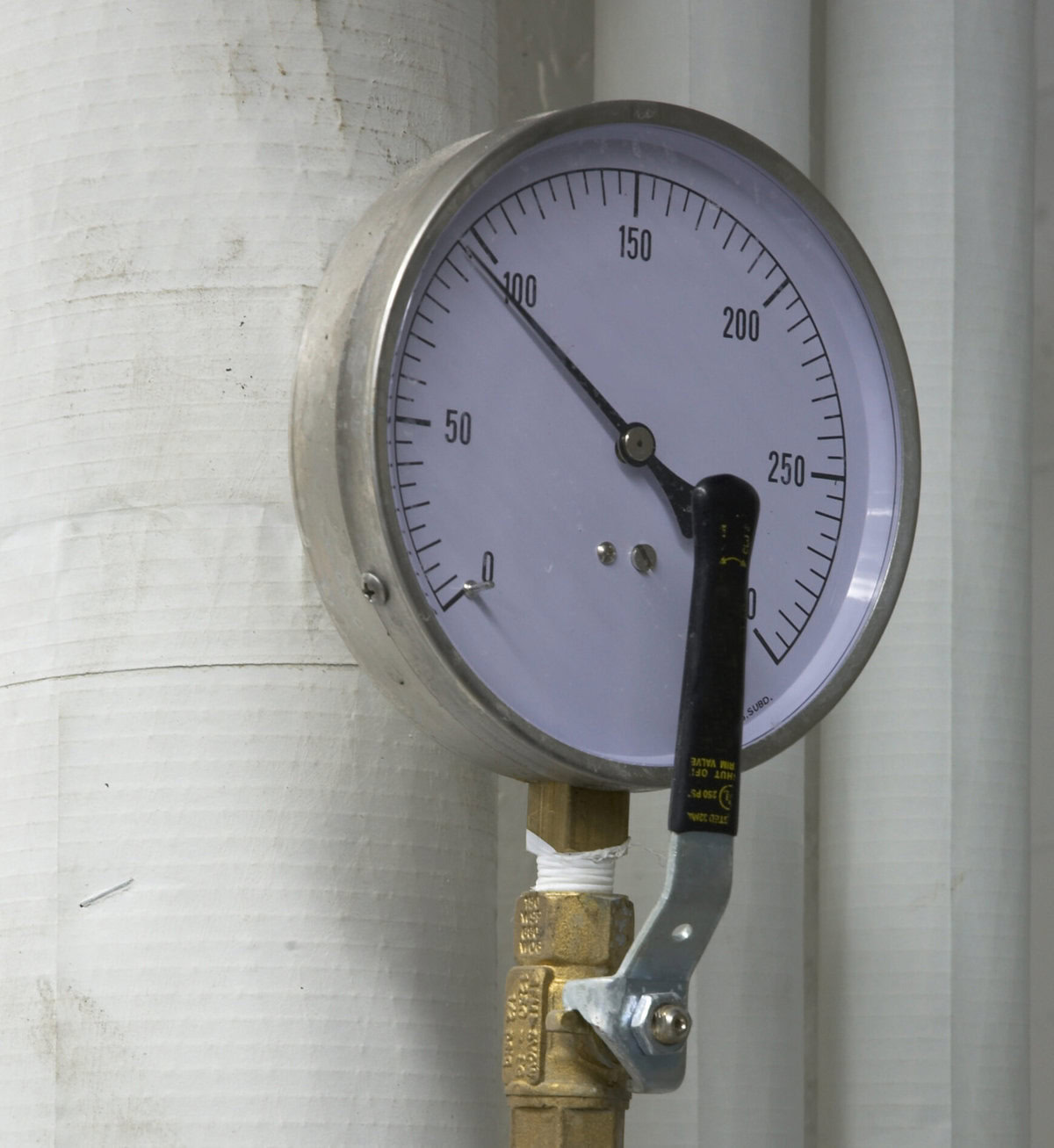 Close-up of a pressure gauge with a black handle attached to a brass pipe.