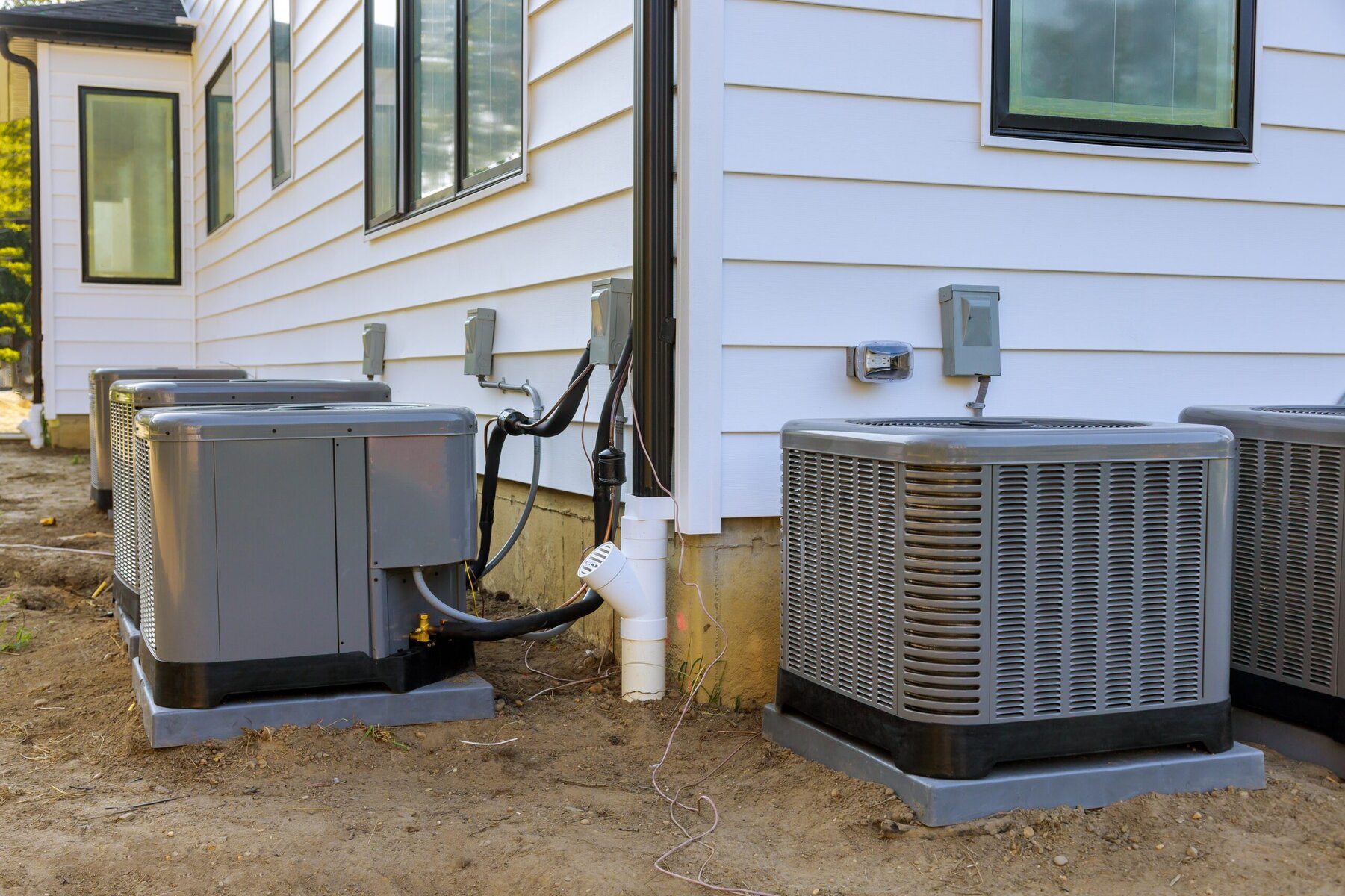 Several outdoor air conditioning units next to a white house under construction.