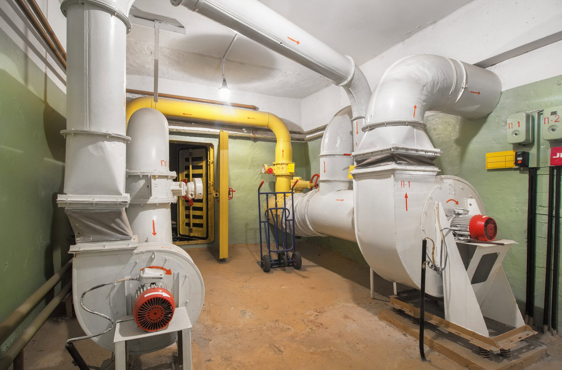 Industrial room with large ventilation pipes, machinery, and a metal door.
