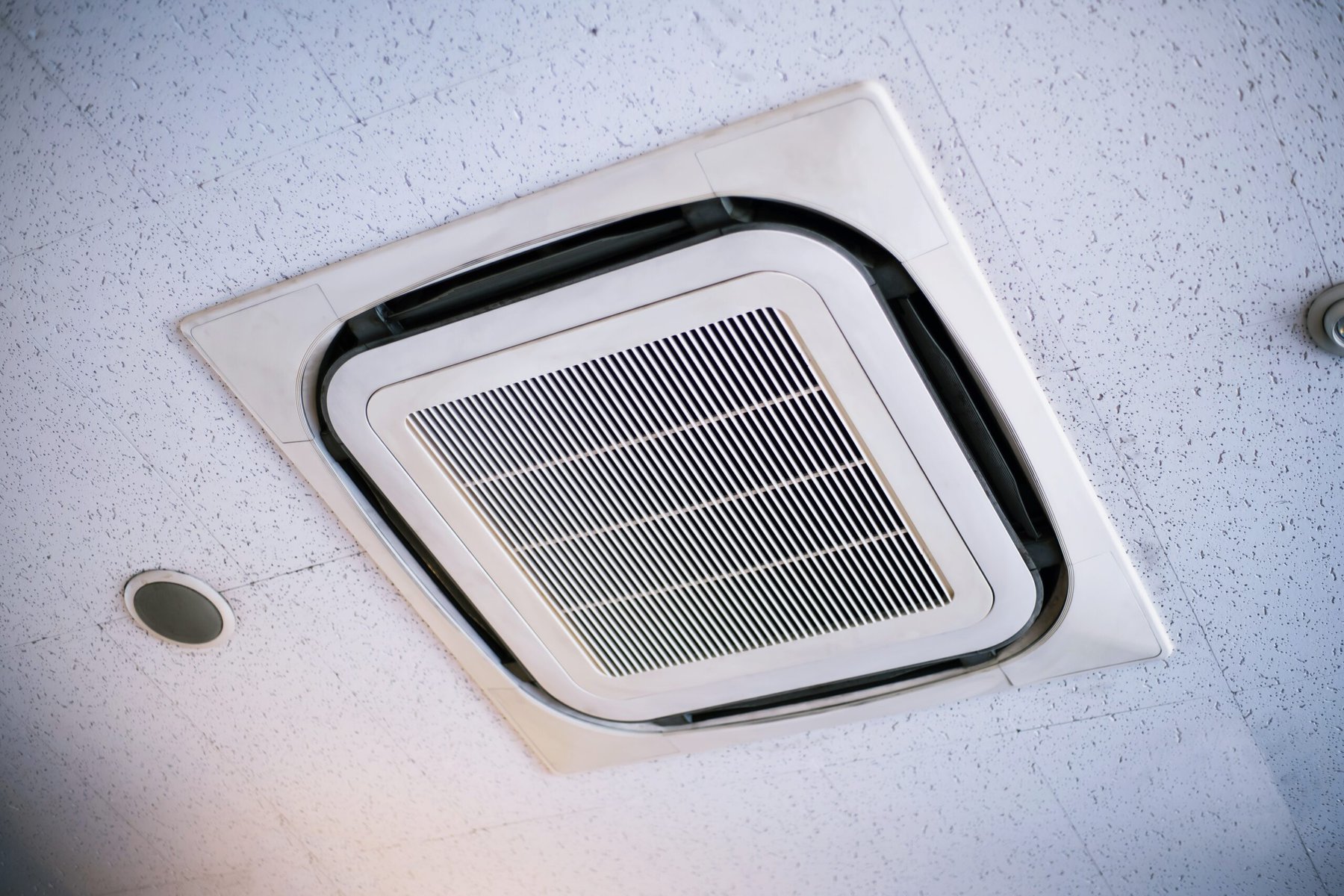 White ceiling-mounted air conditioning unit with a rectangular vent.