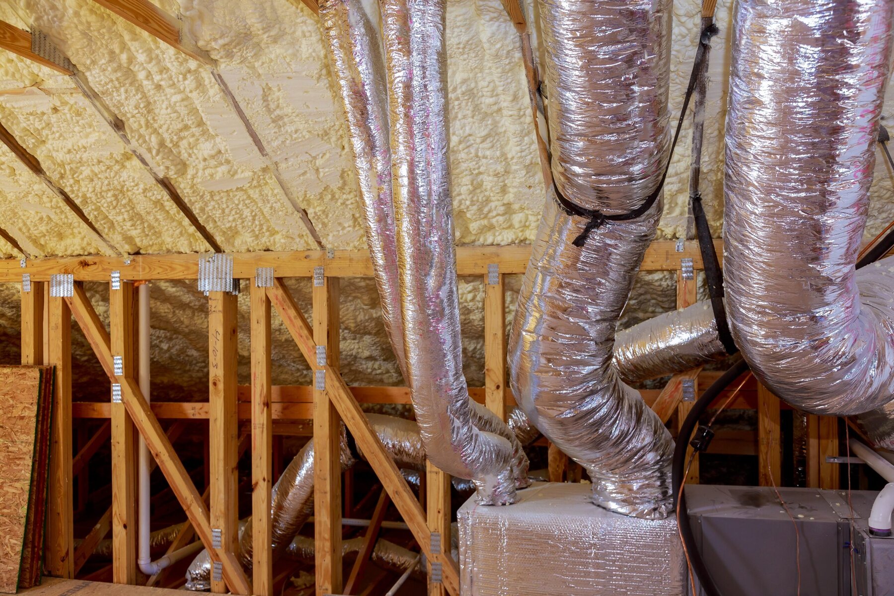 Attic with spray foam insulation, wooden trusses, and silver HVAC ducts