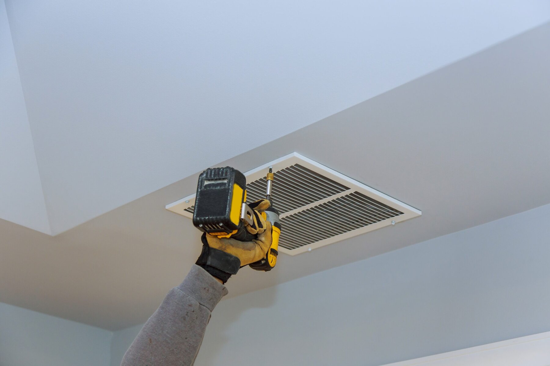 Hand installing an air vent on a white ceiling with a screwdriver