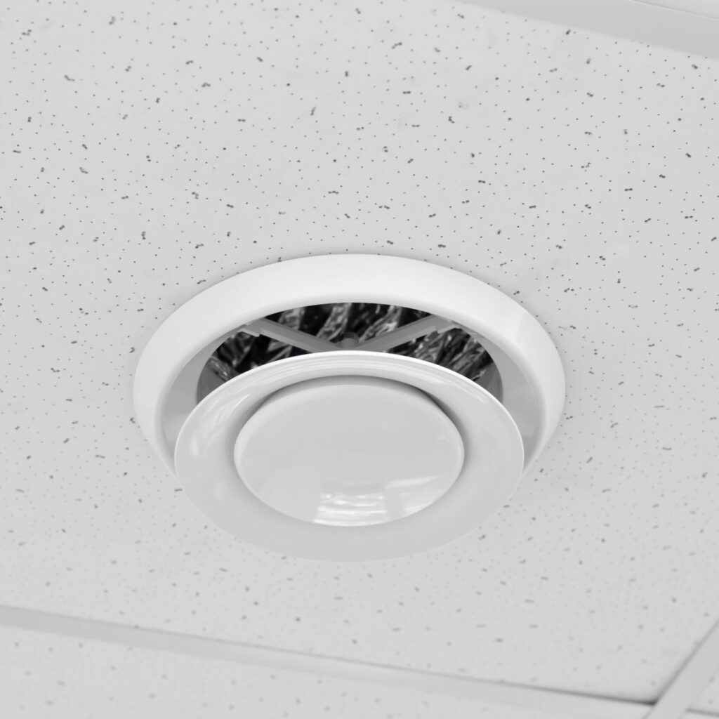 Close-up of a white circular air vent in a speckled ceiling.