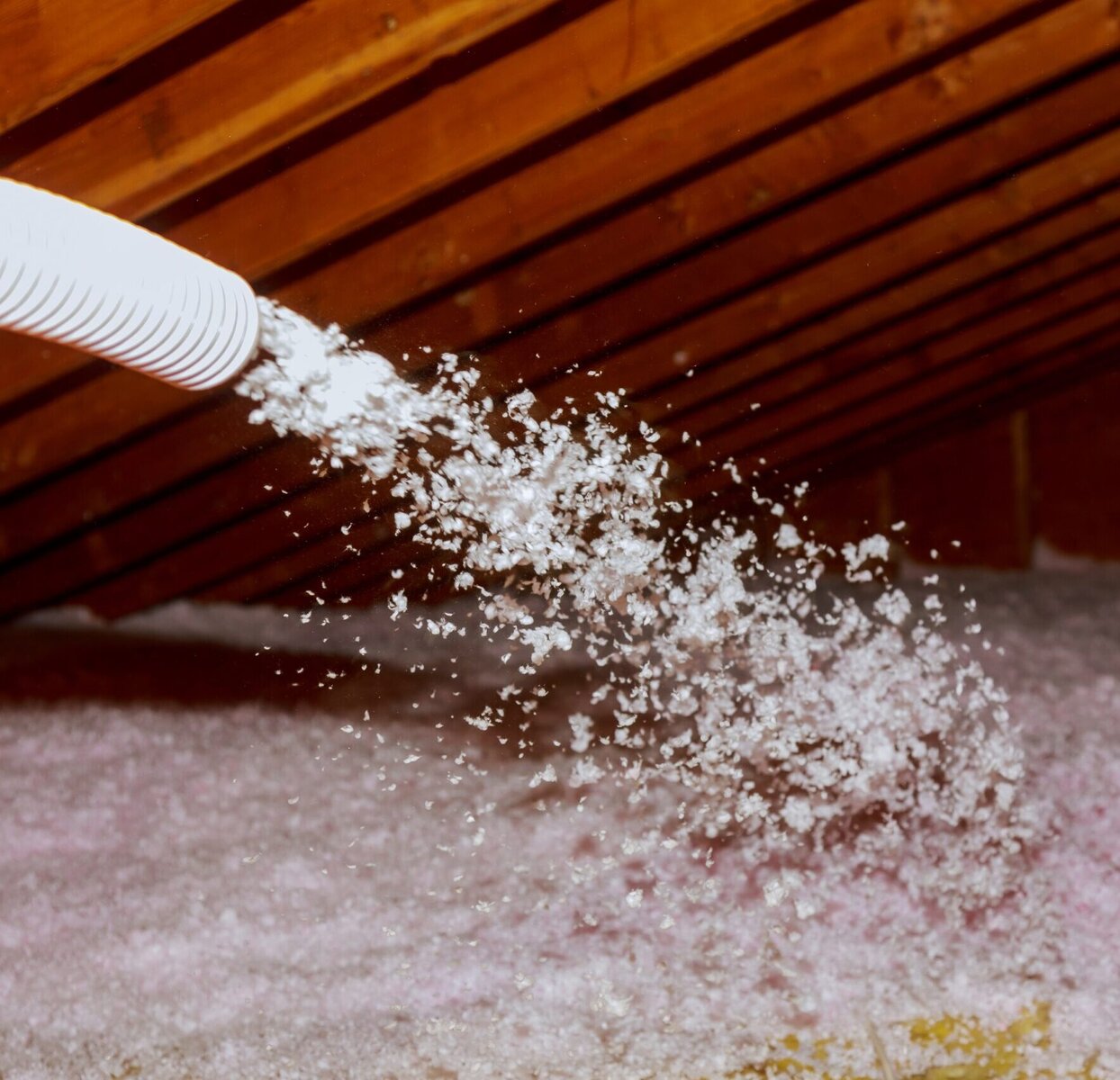 Insulation being blown into an attic with wooden beams visible