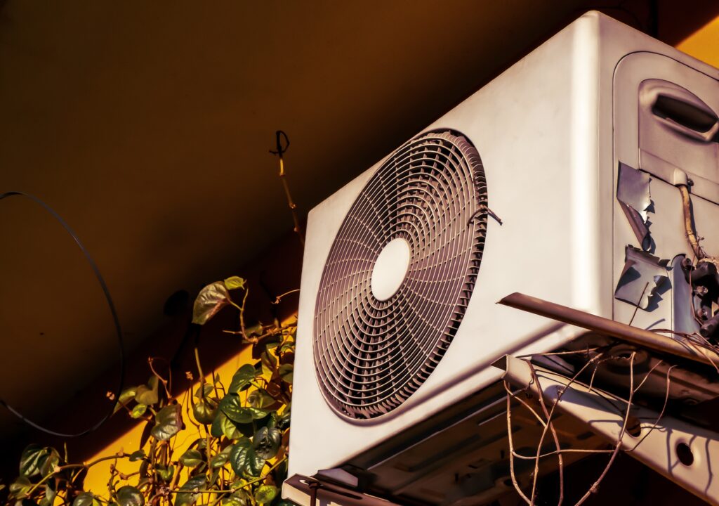 Outdoor air conditioning unit with a large fan and green leaves.