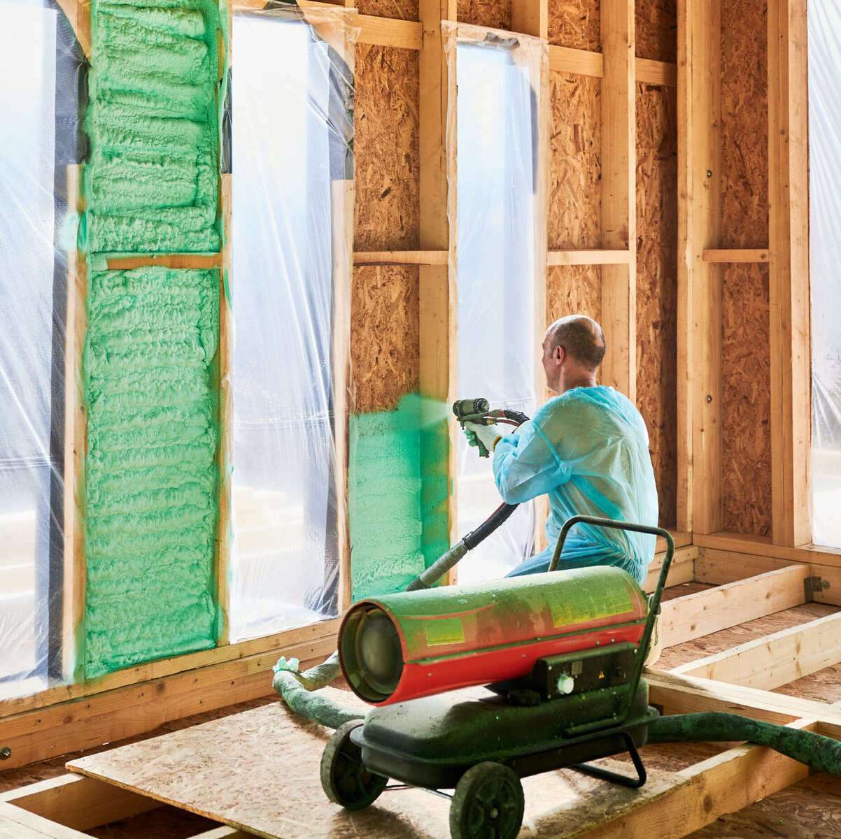 http://Man%20in%20blue%20suit%20spraying%20green%20foam%20insulation%20onto%20wall%20studs