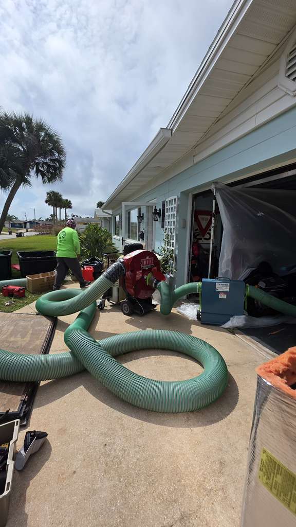 Man working with large green hoses and machinery outside a house.