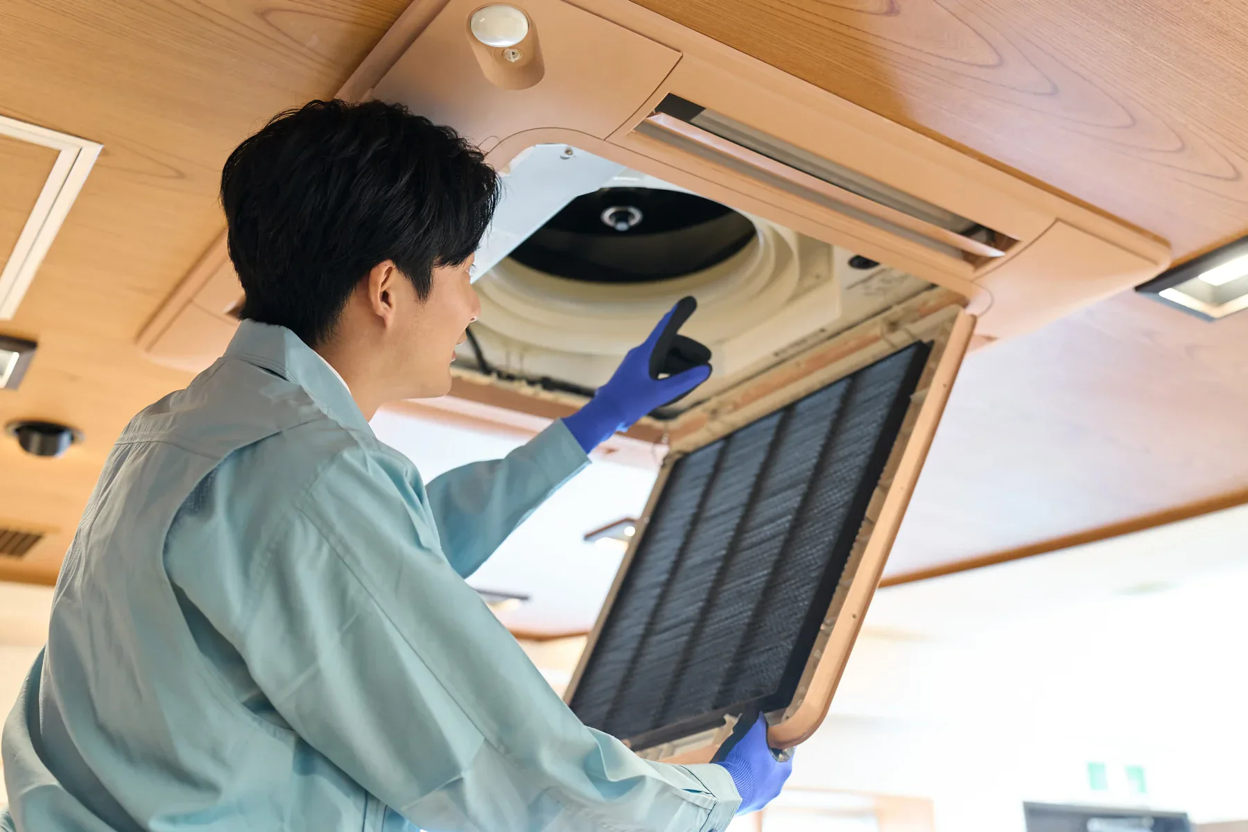 Man in blue gloves cleaning an air conditioning unit filter
