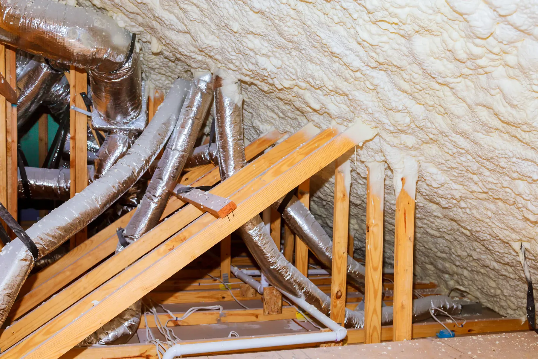 Attic with spray foam insulation, wooden beams, and ductwork
