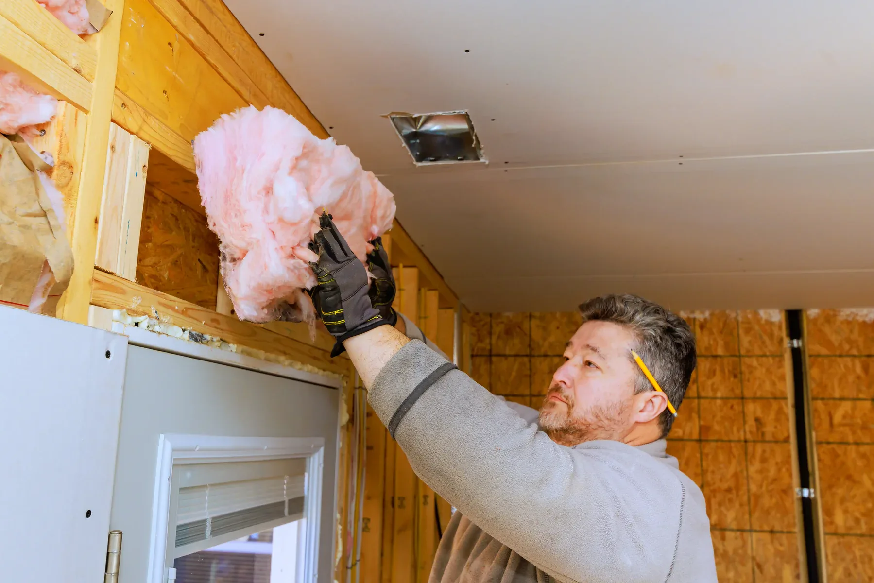 Man installing pink fiberglass insulation in a ceiling