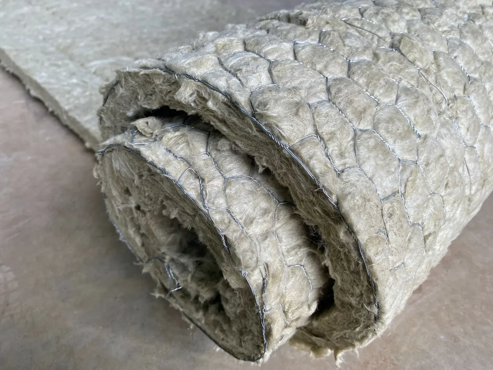Roll of light-colored fibrous insulation with wire mesh visible on the surface.