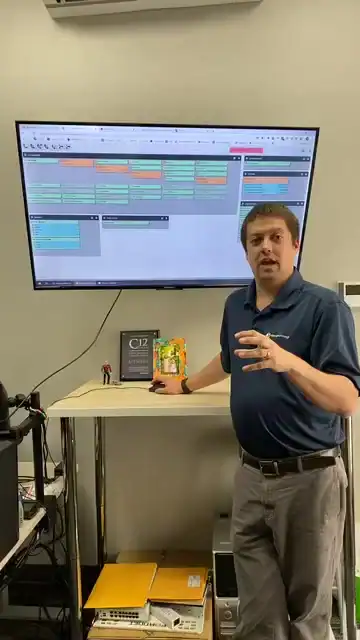 Man presenting in front of a large digital calendar on a screen.